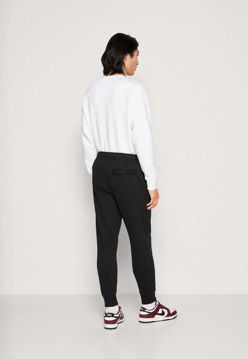 Pantalones de chándal negros con un corte slim, cinturilla elástica y detalle de bolsillo trasero, combinados con zapatillas blancas y burdeos y un sudadera blanca.