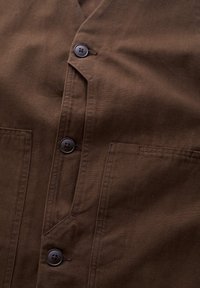 Brązowa koszula na guziki z dwiema przednimi kieszeniami, teksturowany materiał i zapięcie na pięć guzików z ciemnymi, matowymi guzikami z plastiku.