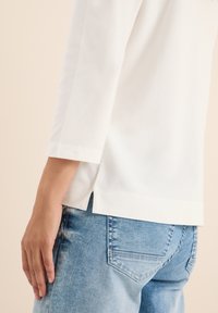 Witte, lange mouw top met een rechte snit en zijsplitten, gecombineerd met lichtblauwe denim jeans met achterzakken en een vervaagde afwerking.