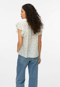 Blouse légère à motifs floraux en blanc, avec des manches volantées et une coupe décontractée, associée à un jean en denim bleu ample.