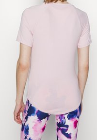 Camiseta atlética de color rosa claro con mangas cortas y dobladillo redondeado, combinada con leggings de patrón colorido en tonos morados y rosas.