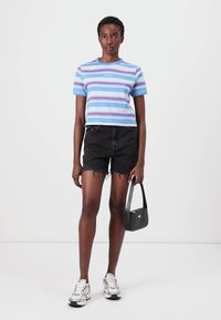 Gestreept blauw T-shirt met korte mouwen en rode en witte accenten, gecombineerd met zwarte denim shorts. Accessoires zijn een kleine zwarte handtas en zilveren sneakers.