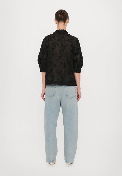 Sort gennemsigtig bluse med blomstermønster, med krave og trekvartærmer. Kombineret med lyseblå højtaljede jeans.