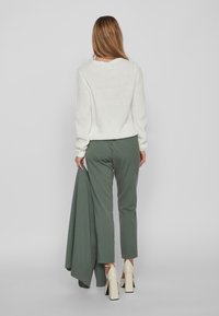 Kreemjas kudumine särk, rohelised voolavad püksid ja heledat tooni kontsad. Tähtsad detailid: mugav lõige, soonikkoes mansetid ja pikk kangas.