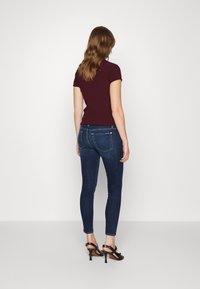 Top ribeteado burdeos con mangas cortas, combinado con jeans ajustados azul oscuro y sandalias de tacón negro. Diseño simple y ajustado, con detalles mínimos.