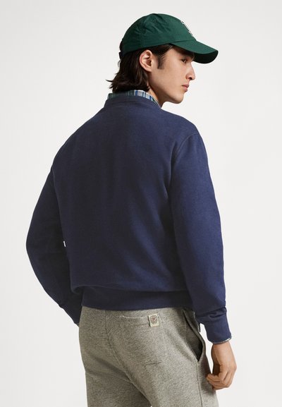 Mörkblå sweatshirt med texturerad yta, rund halsringning och ribbade muddar, kombinerad med ljusgrå byxor med en logotypmärke på baksidan.