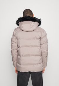 Jasno beżowa kurtka puchowa z czarnym kapturem z futra ekologicznego, pikowany wzór, elastyczne mankiety i luźny krój, widok z tyłu.