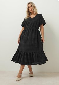 Musta, teksturoidulla keskipitkä mekko, jossa on V-pääntie, puffihihat, kapea vyötärö ja röyhelöhelma, valmistettu kevyestä kankaasta.