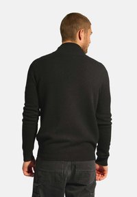 Czarny sweter z dzianiny z ściągaczem u dołu i na mankietach, z klasycznym okrągłym dekoltem i miękką teksturą, przedstawiony z tyłu.