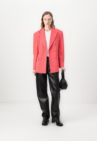 Dubbele blazer in levendig koraal, gemaakt van gestructureerde stof, gecombineerd met hoge zwarte neplederen broeken en een kleine zwarte handtas.