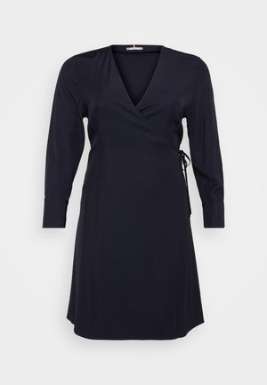 Mornarskoplavi šalovi haljina s dugim rukavima, V-izrezom i detaljima vezivanja sa strane. Izrađena od glatkog, laganog materijala s lagano drapiranim oblikom.