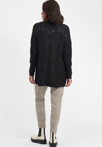 Svart stickad tröja med ett texturerat mönster, långa ärmar och en avslappnad passform. Matchat med rutiga byxor och ankelstövlar.