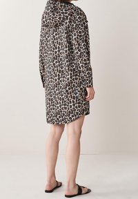 Leopardprintkjole med hætte, lange ærmer og en buet kant. Lavet af let stof med en blanding af brun, sort og creme.