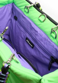Interieur van een groene en paarse tote bag, met een paarse stoffen voering, een ritsvak, metalen hardware en contrasterende afwerkingsdetails.