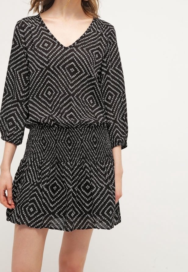 Černé vzorované šaty s výstřihem do V, 3/4 rukávy a nařaseným pasem. Obsahují bílé geometrické diamantové tvary po celé látce.