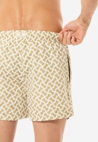 Pantaloni da bagno corti in un motivo geometrico beige e crema, con vita elastica e tasche laterali.