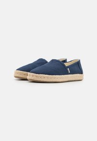 Navy canvas slip-on kengät, joissa on punottu juteepohja, pyöristetty kärki ja minimaalinen ompelutaito yläosassa.