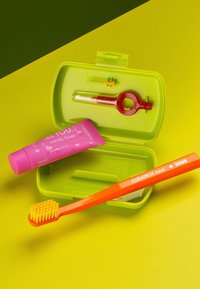 Curaprox reseborste i orange, grönetui, rosa tandkrämstube, röd verktyg och gula borst, mot en gul bakgrund.