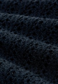 Donkertextiel met reliëf, lusvormige en geperforeerde patronen die een zachte, tastbare oppervlakte creëren met lichte plooien en schaduwen.