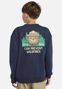 Marinelblauwe sweatshirt met ronde hals, featuring een beer graphic en de tekst "Jij alleen kunt bosbranden voorkomen" tegen een achtergrond van bomen in groen en crème.
