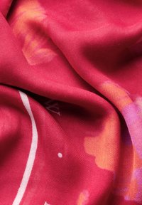 Textiel sjaal in felroze met vage oranje en paarse patronen. Zachte, gestructureerde stof met een subtiele glans en witte ontwerpelementen.