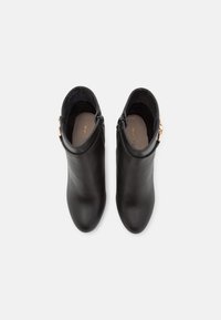 Botas de cuero negro hasta el tobillo con un acabado suave, punta redonda y cremallera lateral. Presenta un pequeño acento dorado en el tirador de la cremallera.