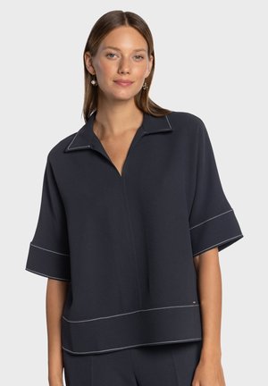 Granatowa bluzka z krótkim rękawem i kołnierzykiem, z białymi przeszyciami i luźnym krojem. Gładka faktura materiału.