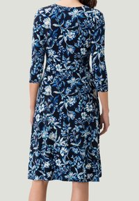 Vestido marino con mangas tres cuartos, que presenta un patrón floral en blanco y azul. Hecho de una tela suave, tiene un corte holgado y una longitud hasta la rodilla.
