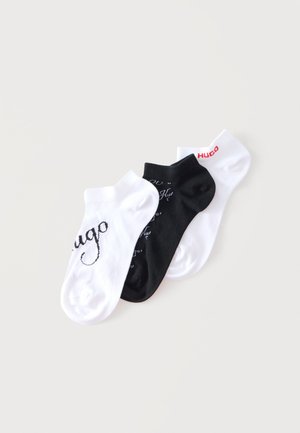 Tre calzini bassi in bianco, nero e bianco, ciascuno con il nome del marchio "Hugo" in stili e colori diversi.