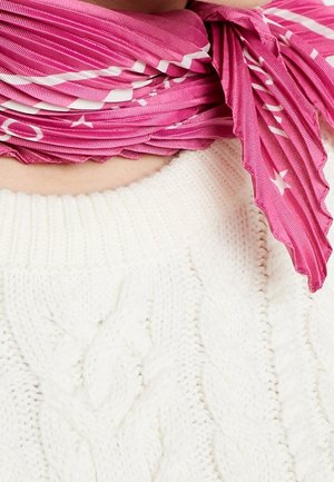 Primer plano del escote de un suéter blanco de punto trenzado con una bufanda rosa plisada con estrellas blancas atada alrededor del cuello.