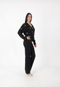 Svart stickad cardigan med hjärtformade utsmyckningar, tillsammans med svarta höga byxor. Skorna är i krämfärgad med en strukturerad mönstring.