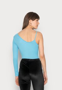 Bodysuit assimétrico de manga longa em tecido canelado azul claro com costas em V, combinado com calças pretas de veludo de cintura alta.