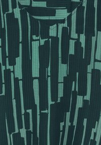 Tessuto testurizzato in teal e verde scuro, con motivi astratti a pennellate verticali. Collo semplice con dettagli di cucitura discreti.