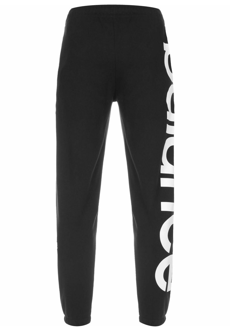 Pantalons de survêtement noirs avec une taille élastique, présentant un grand logo blanc imprimé verticalement le long de la jambe gauche. Matière en coton doux.