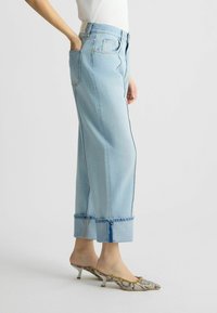 Jeans de culoare albastră deschisă, cu talie înaltă și croială dreaptă, cu tiv mediu și cusături contrastante, asortați cu mocasini cu toc cu un model.