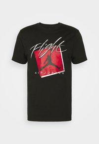 T-shirt noir Air Jordan avec le texte blanc « Flight », fond carré rouge et silhouette noire d’un joueur de basketball en train de sauter.