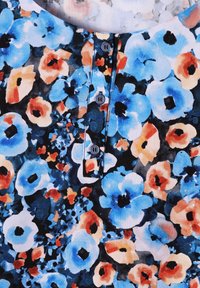 Tessuto di blouse floreale con motivi blu, arancione e nero; scollatura rotonda con patta a quattro bottoni; texture morbida e colori vivaci.
