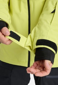 Felgeel waterdicht jack met verstelbare klittenbandmanchetten, zwarte binnenvoering en een gestroomlijnd ontwerp met minimale hardware.