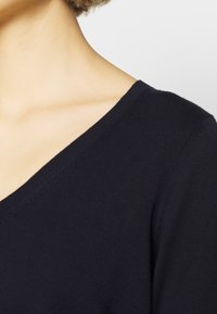 Granatowy sweter dzianinowy z głębokim dekoltem w serek, charakteryzujący się gładką teksturą i starannym szwem wzdłuż krawędzi.