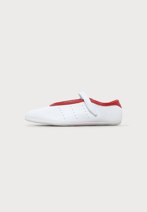 Chaussure plate blanche avec bordure et sangle rouges, petits trous perforés sur le côté, présentée sur un fond clair uni.