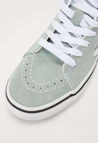 Jasnozielone zamszowe sneakersy z białymi sznurowadłami, gumową podeszwą, perforowanymi detalami oraz białym przeszyciem wzdłuż brzegów i czubka.