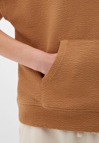 Hnědá texturovaná mikina s přední kapsou a žebrovaným spodním lemem. Látka má měkký, mírně vystouplý vzor.