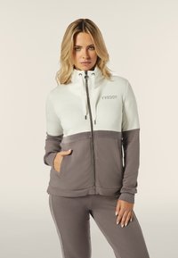 Giacca a zip in grigio chiaro e grigio scuro. Caratterizzata da colletto alto, chiusura a zip frontale, tasche anteriori e dettaglio con logo. Tessuto morbido e design aderente.