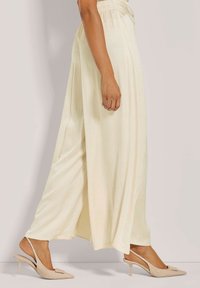 Vloeiende ivoorkleurige maxi-rok van lichtgewicht stof, met een smocktail en zijslits, gecombineerd met beige slingback hakken.