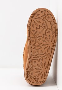 Botte en daim marron avec une semelle en caoutchouc à motif présentant des designs géométriques. Étiquette de taille 37 sur la semelle, surface texturée pour une meilleure adhérence.