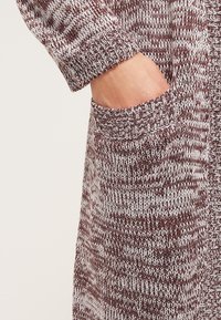 Cardigan lavorato a maglia in marrone e crema con un motivo testurizzato, dotato di una tasca frontale e polsi a costine. Materiale morbido e caldo.