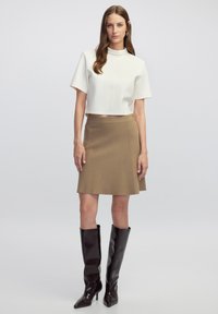 Top blanco corto con mangas cortas, falda beige en línea A y botas negras hasta la rodilla. Textura suave con un ajuste entallado.