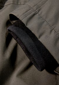 Olivengrønt stof med en glat overflade har en sort elastisk manchet. Syningen er pæn og fremhæver manchettens tætte pasform.