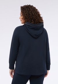 Felpa con cappuccio blu navy, a maniche lunghe, con un taglio rilassato e cuciture a contrasto. Presenta un tessuto morbido e testurizzato.
