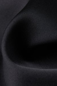 Tela negra con una textura suave, cayendo con delicadeza. El tejido parece fino y uniforme, creando una superficie elegante y refinada.